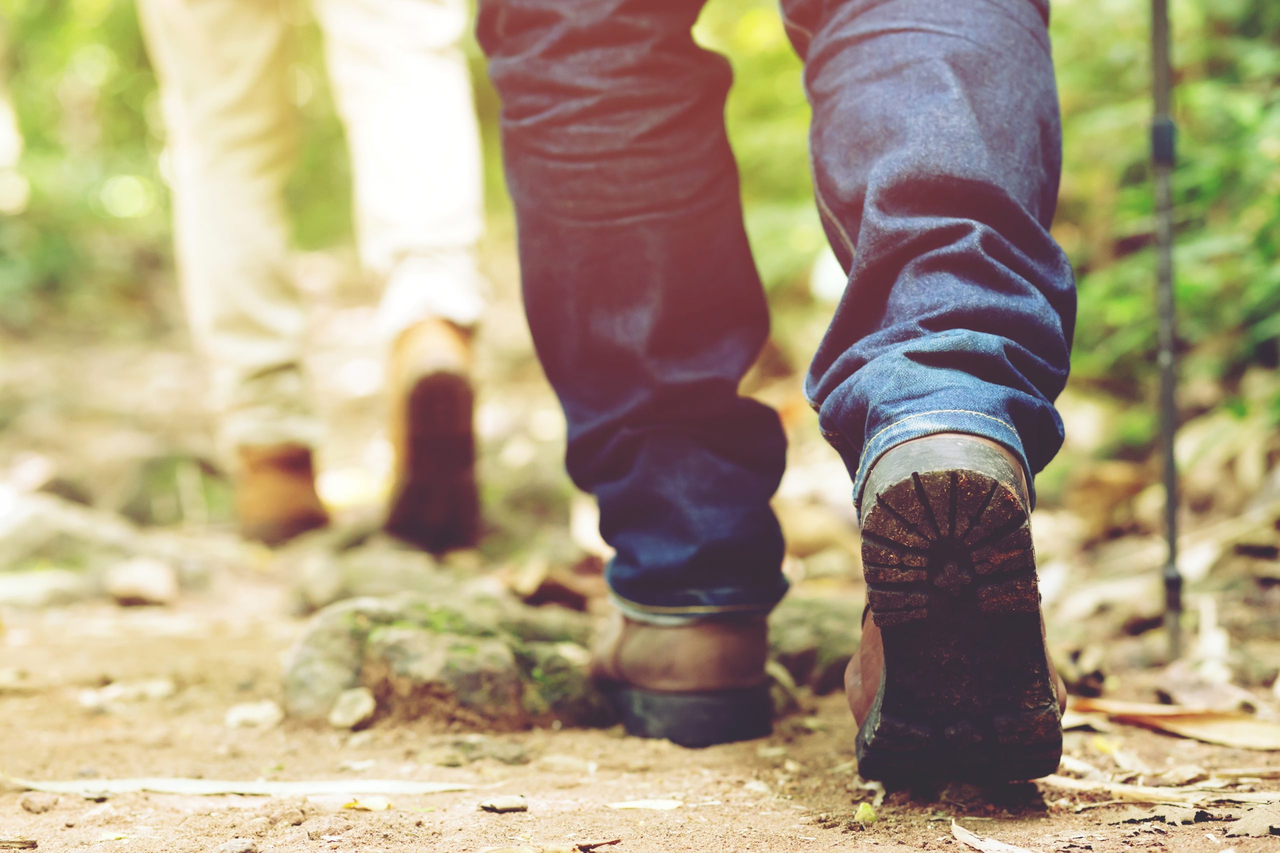 Hiking trail path in action on a mountains or forest with hiking shoes. male and female hikers shoes. are walking through forest path wearing mountain boots and walking sticks. Destination Experience